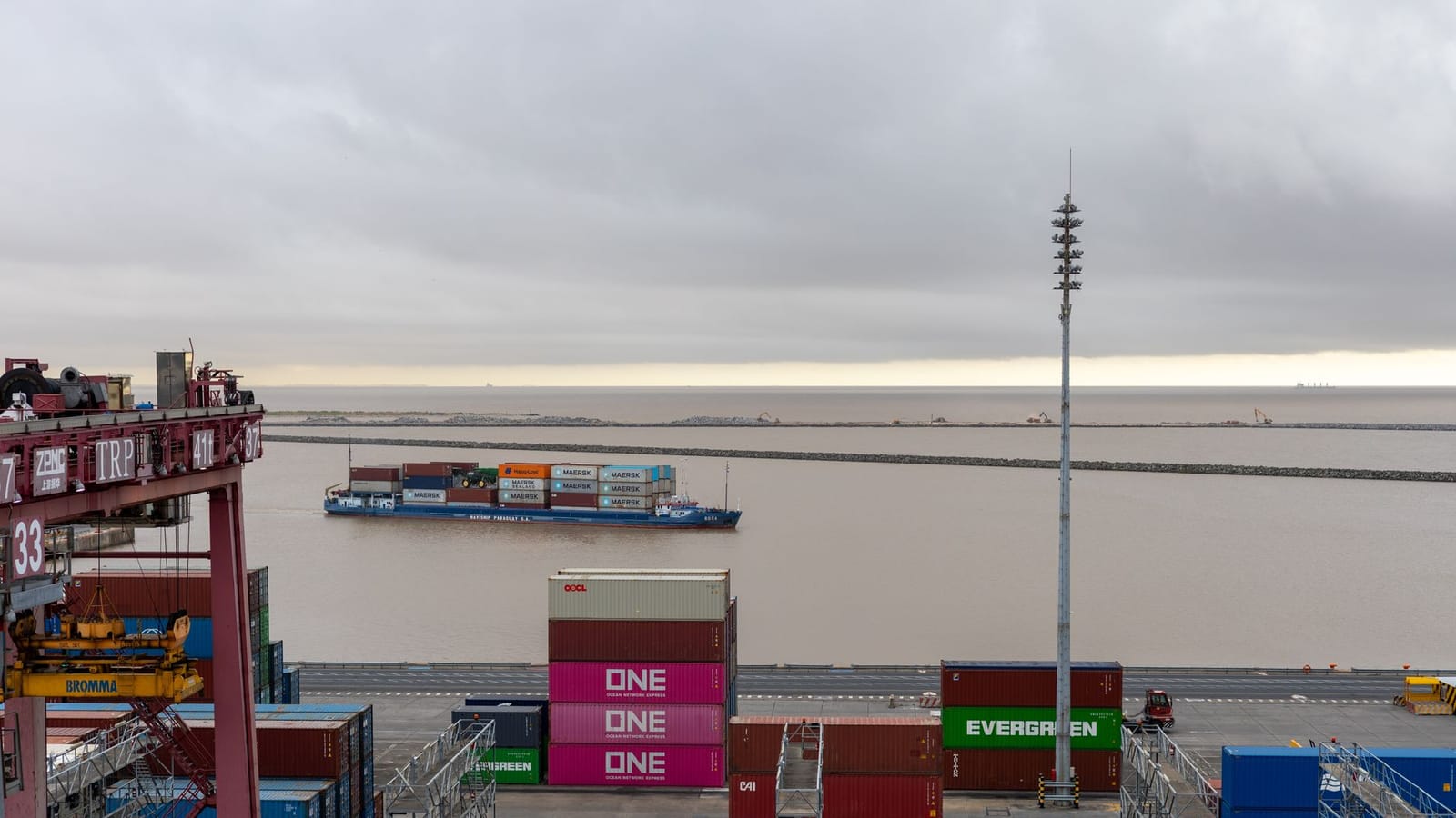 Container ship at a busy cargo port with rows of colorful containers and overcast weather.