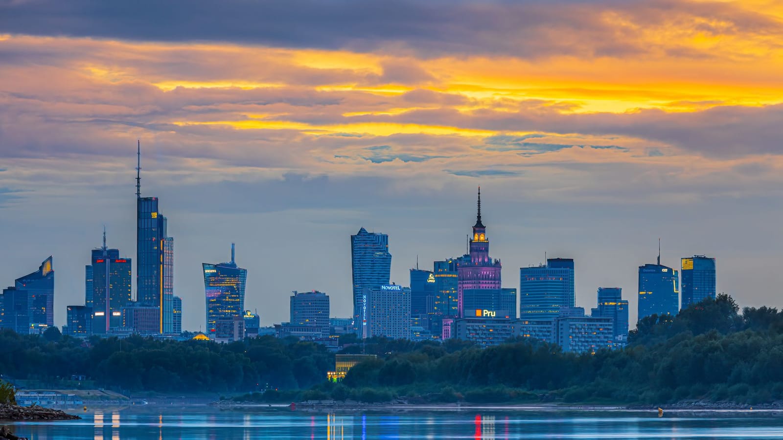 Experience the vibrant Warsaw skyline at sunset, reflecting beautifully in the river.