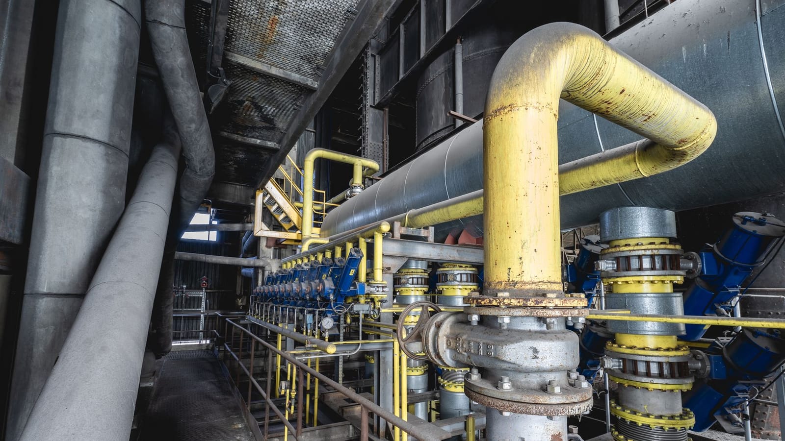 Close-up of an intricate industrial pipeline system featuring yellow valves and steel structures inside a factory.