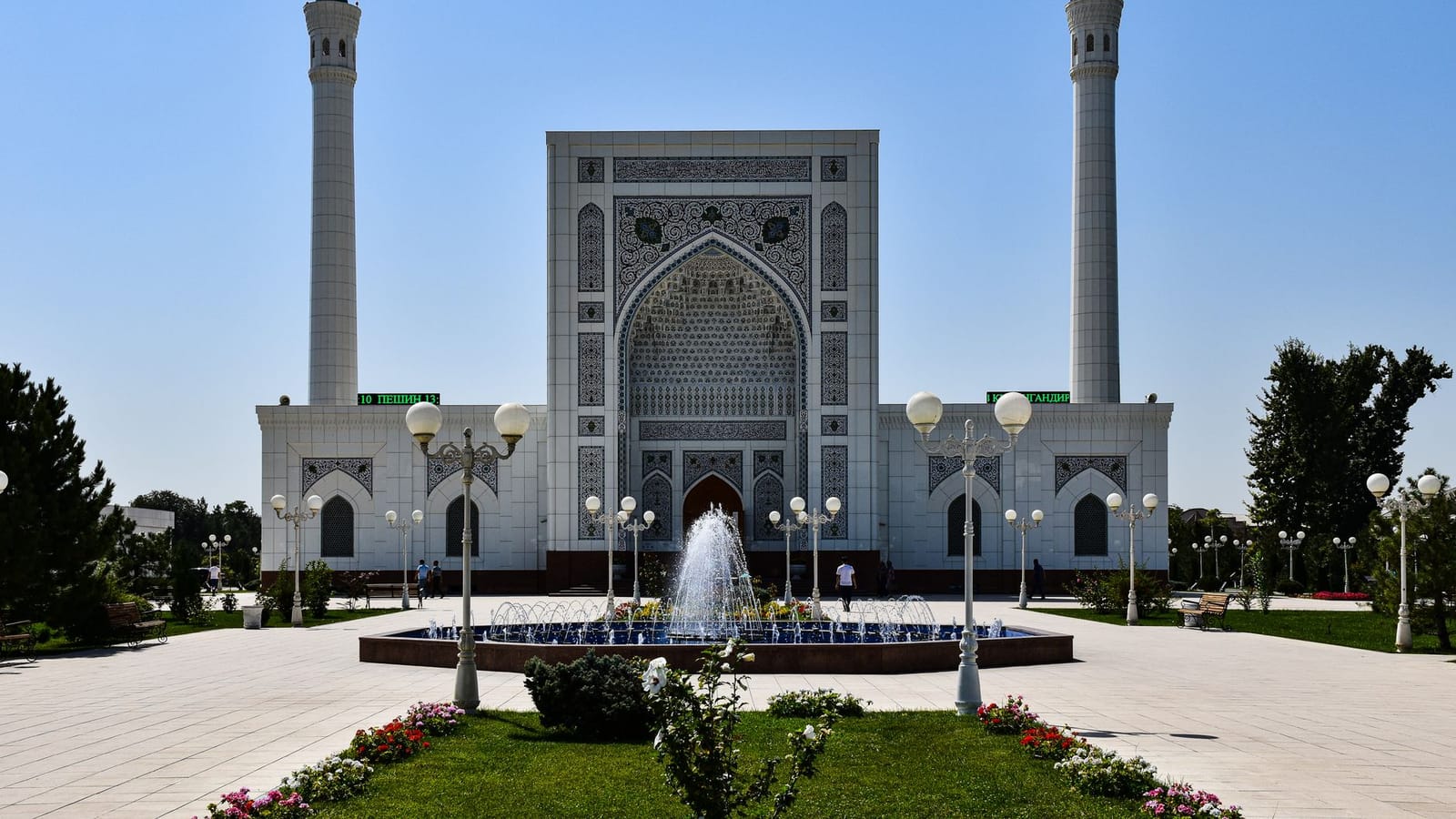 Beautiful mosque with intricate design and fountains under a clear blue sky.
