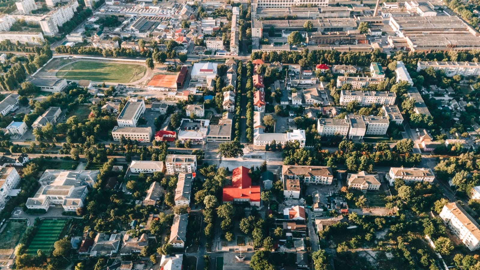 Aerial panorama of a town featuring buildings, streets, and green landscapes from above.