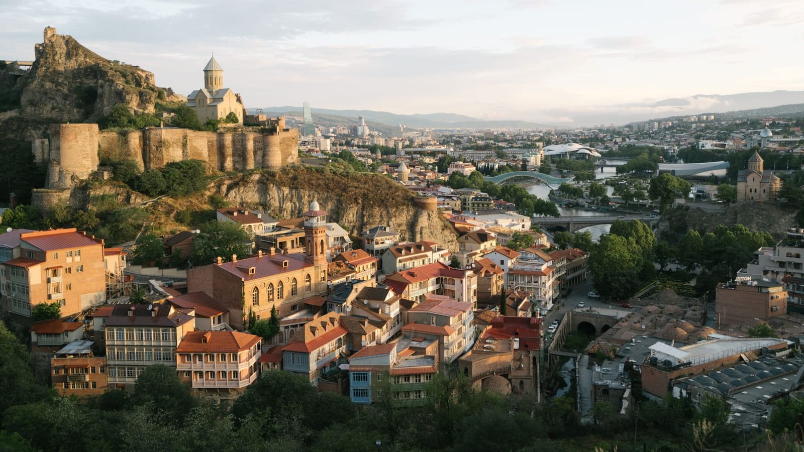A scenic aerial view of Tbilisi featuring the historic Narikala Fortress at sunset.