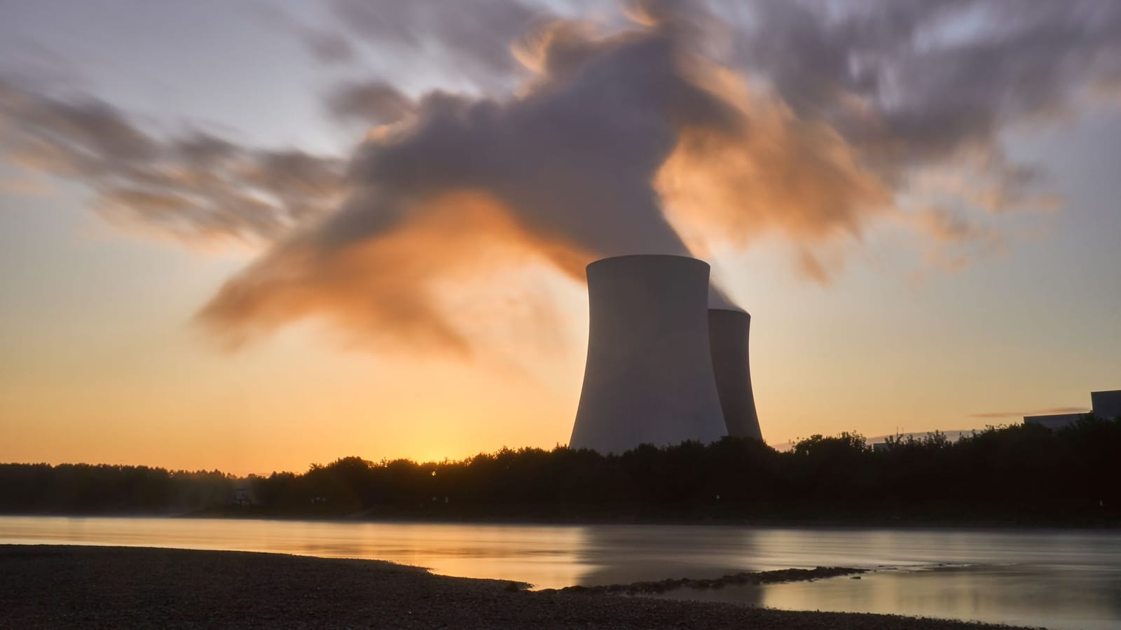 Dramatic image of a nuclear power plant at sunrise with steam rising into a colorful sky.