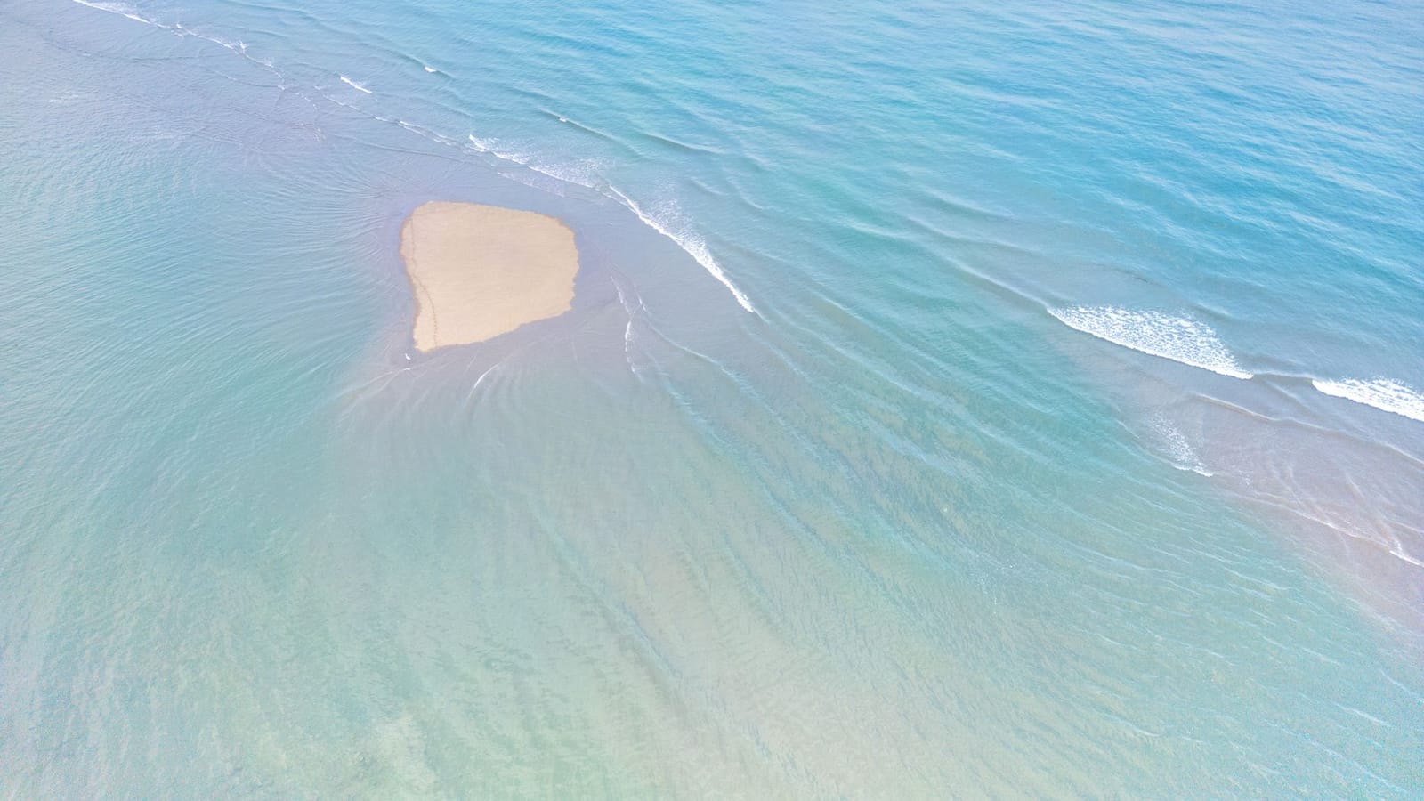 Drone captures a sandy shoal surrounded by clear turquoise waters, highlighting serenity.