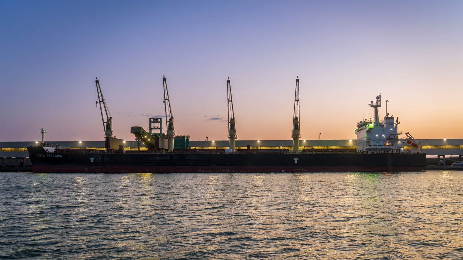 A bulk carrier alongside cranes at sunset, the class of vessel the Caspian trans-shipment route depends on.