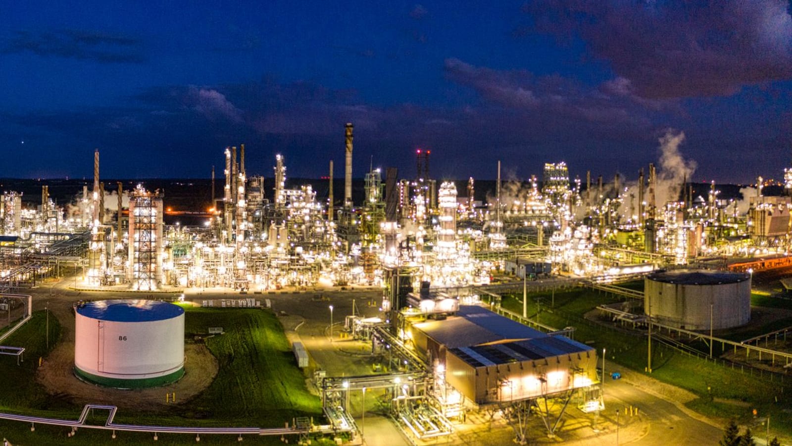 An oil refinery lit at night, the point in the fuel chain the Polish windfall levy is charged on.