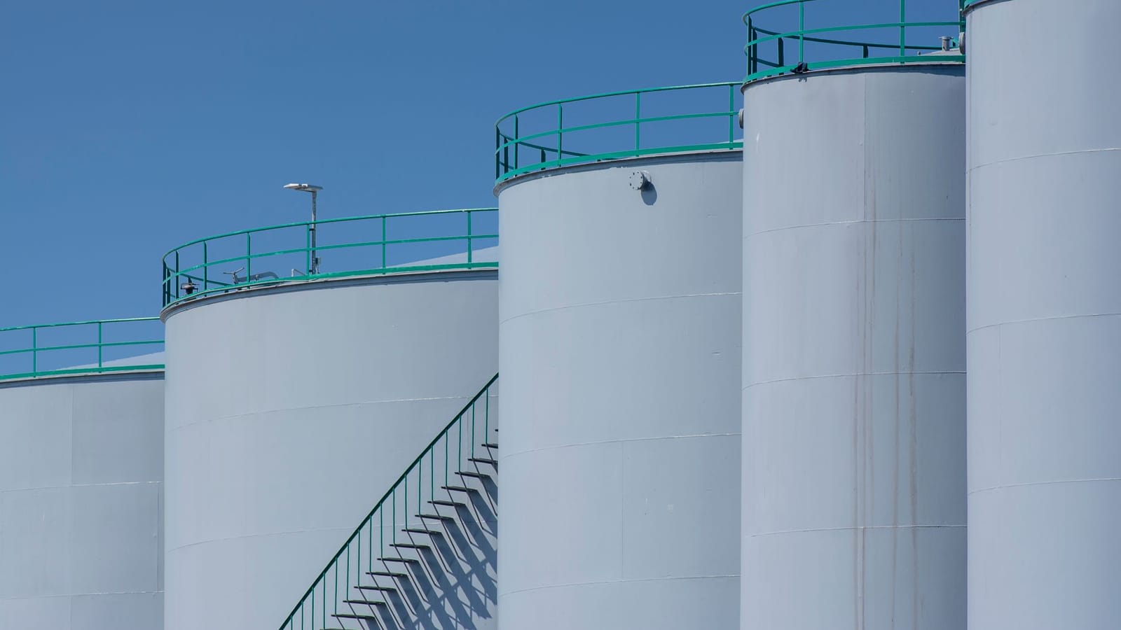 Large industrial storage tanks with green railings against a clear blue sky.