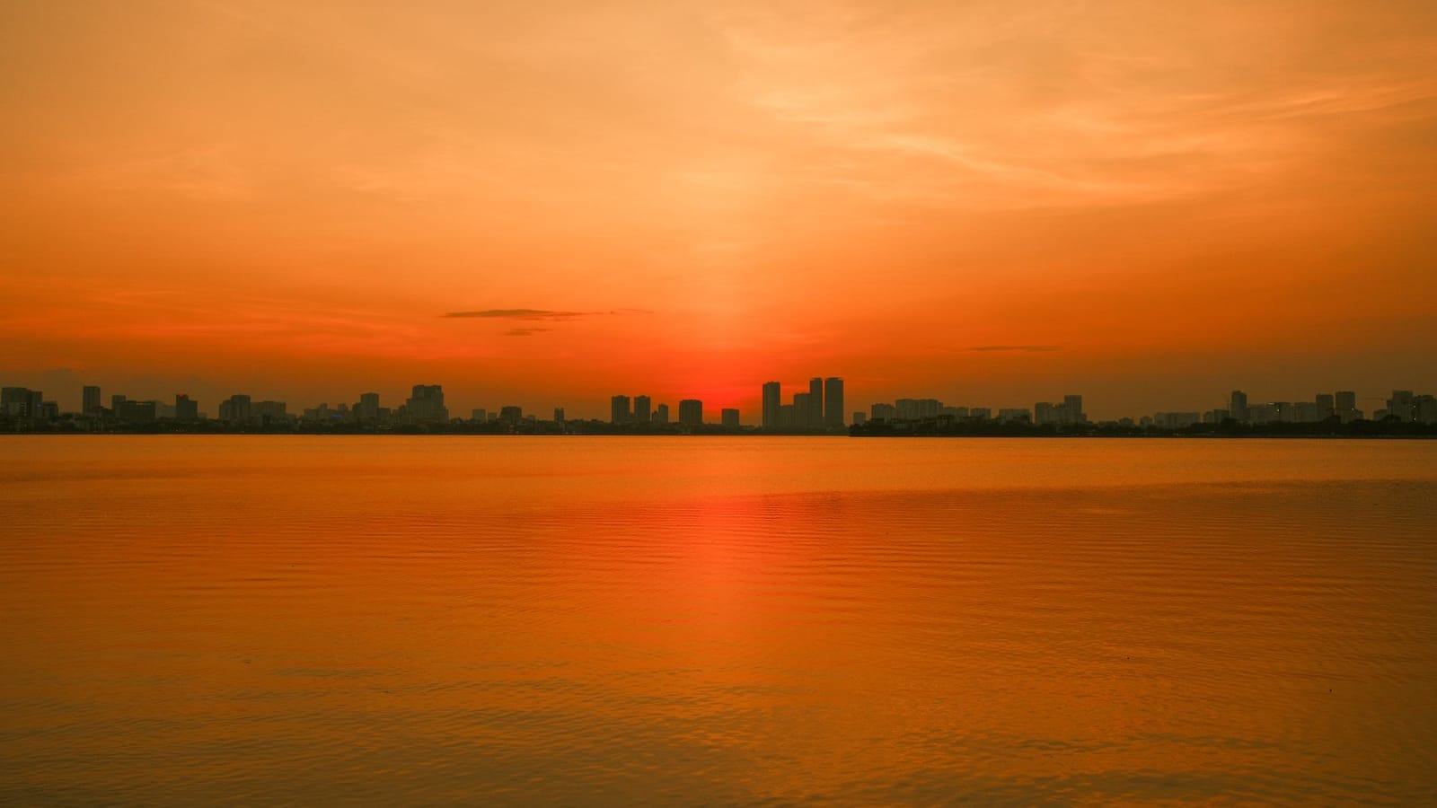 A vivid sunset casts a golden hue over the serene waters of Hanoi, Vietnam.
