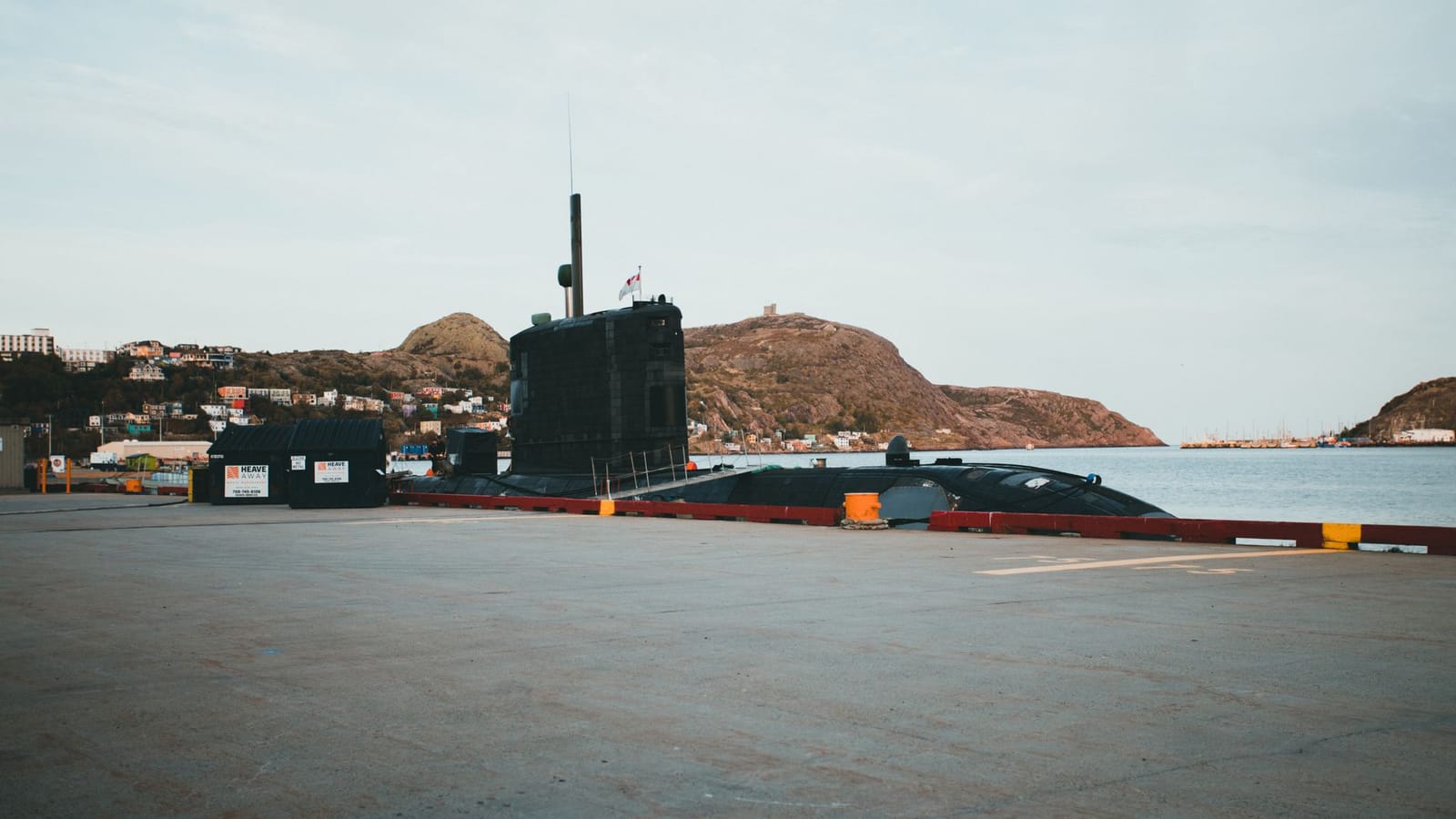 A submarine docked at a pier, surrounded by picturesque hills and calm waters.