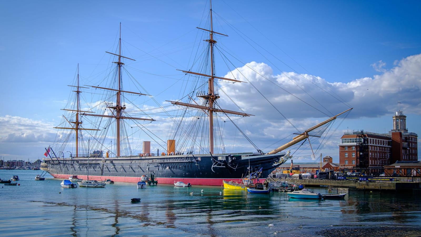 The iconic HMS Warrior, a 19th-century warship, docked in Portsmouth under a clear blue sky.