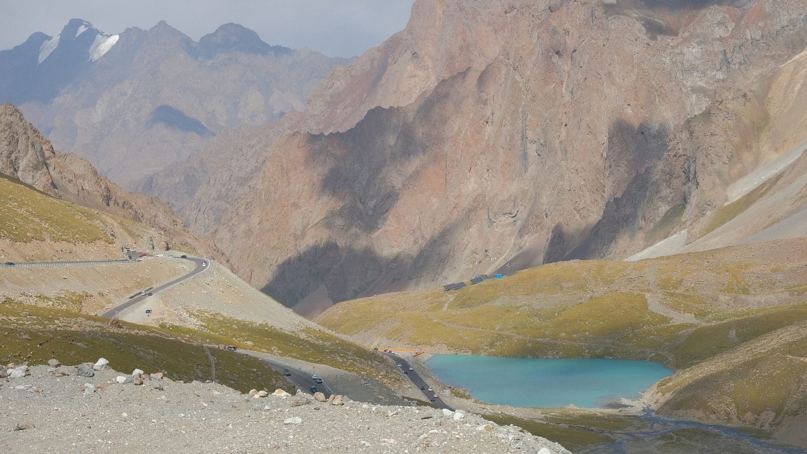 Scenic view of a mountain road with a stunning turquoise alpine lake and rocky terrain.