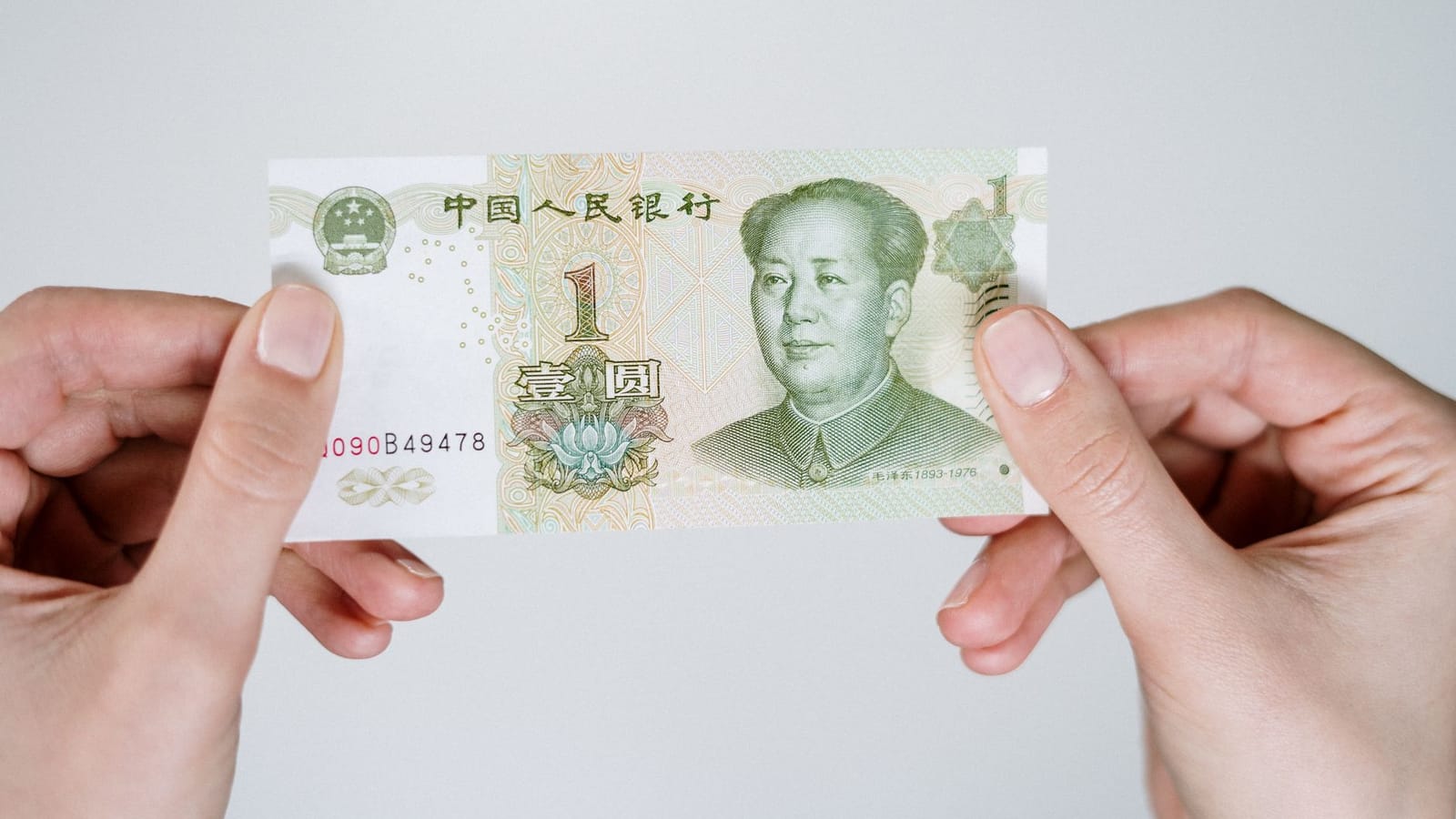 Close-up of hands holding a one Chinese Yuan note, showcasing currency details.