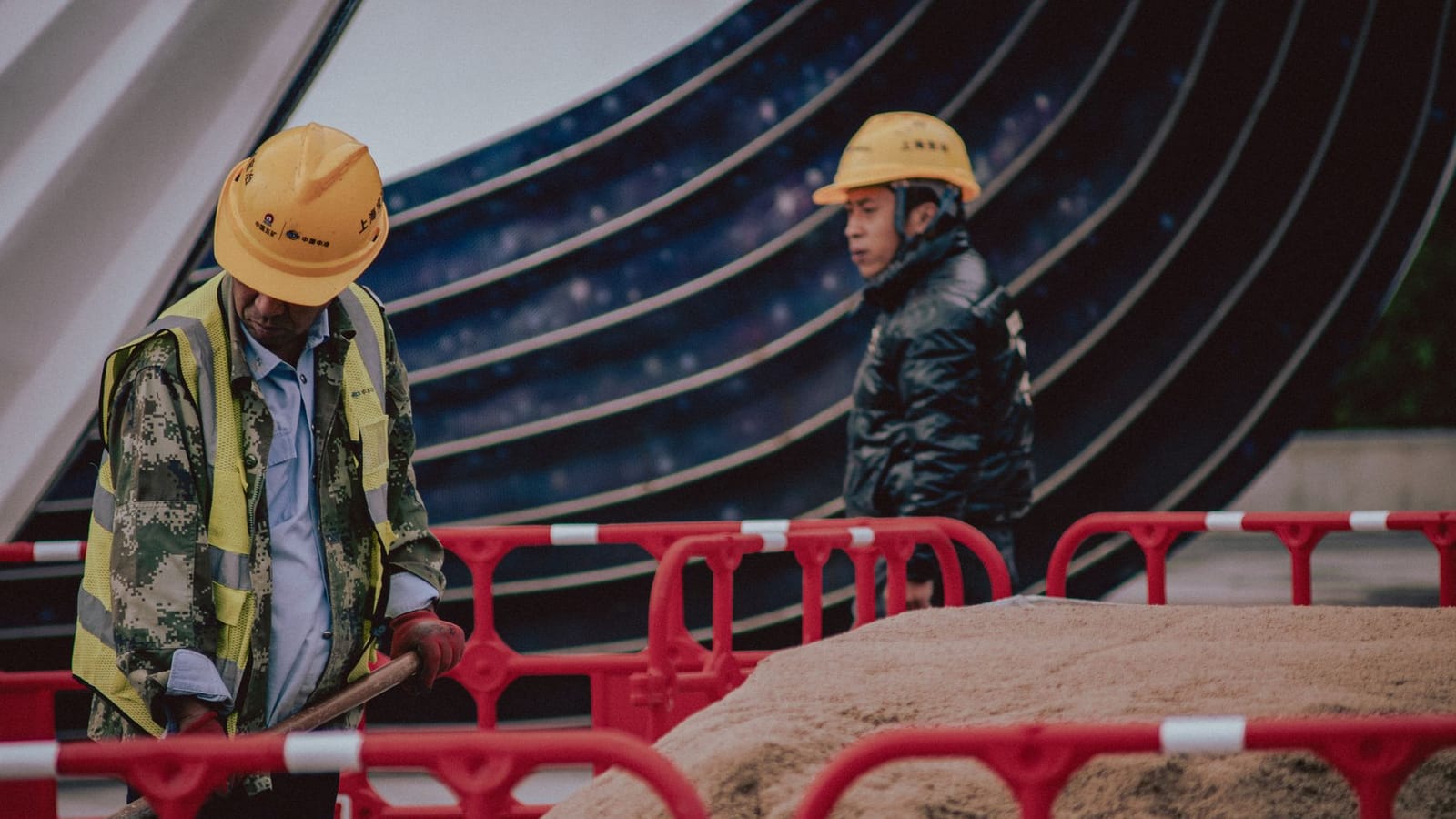 Construction workers with safety gear managing a sand pile outdoors on an urban site.