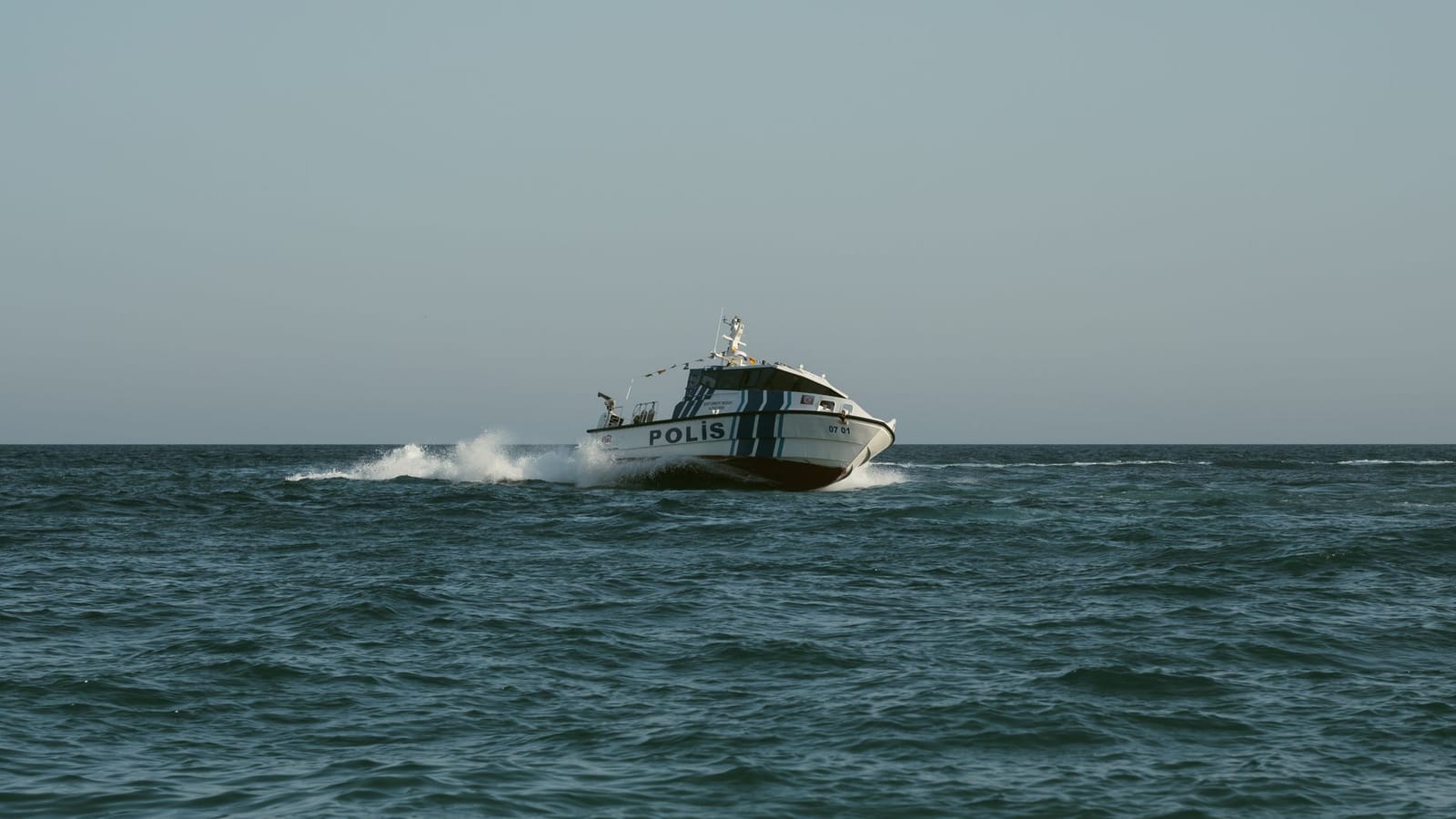 A police boat speeds across the open sea under clear skies, maintaining maritime security.