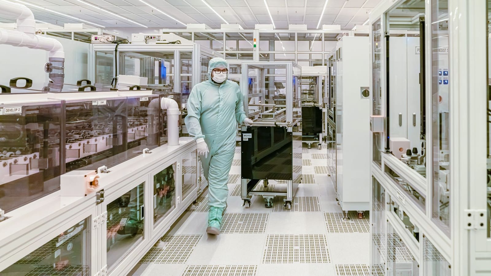 Scientist in protective gear walking in a high-tech cleanroom laboratory environment.