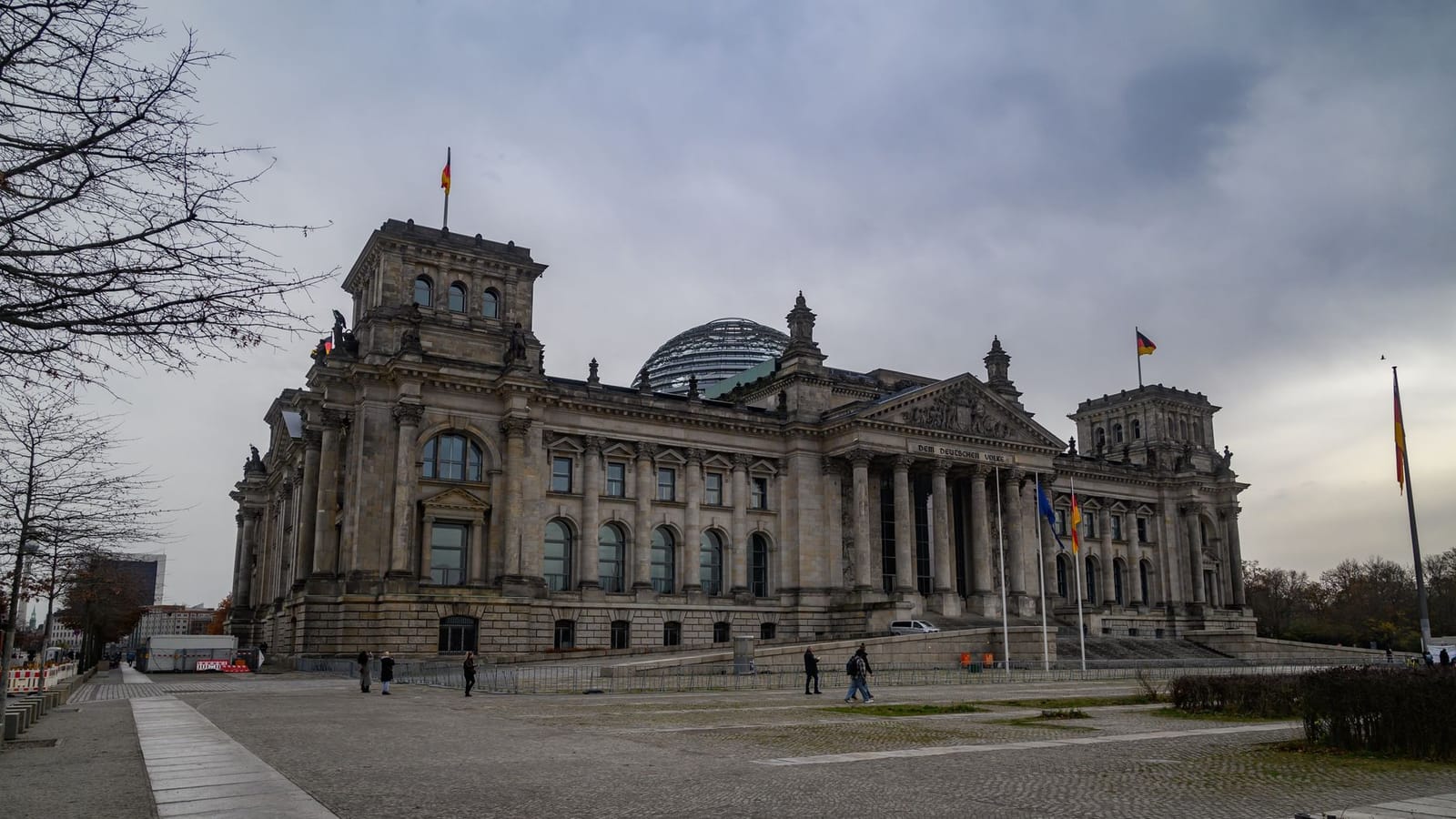 View of the iconic Reichstag building in Berlin under a cloudy sky, featuring its distinctive glass dome.
