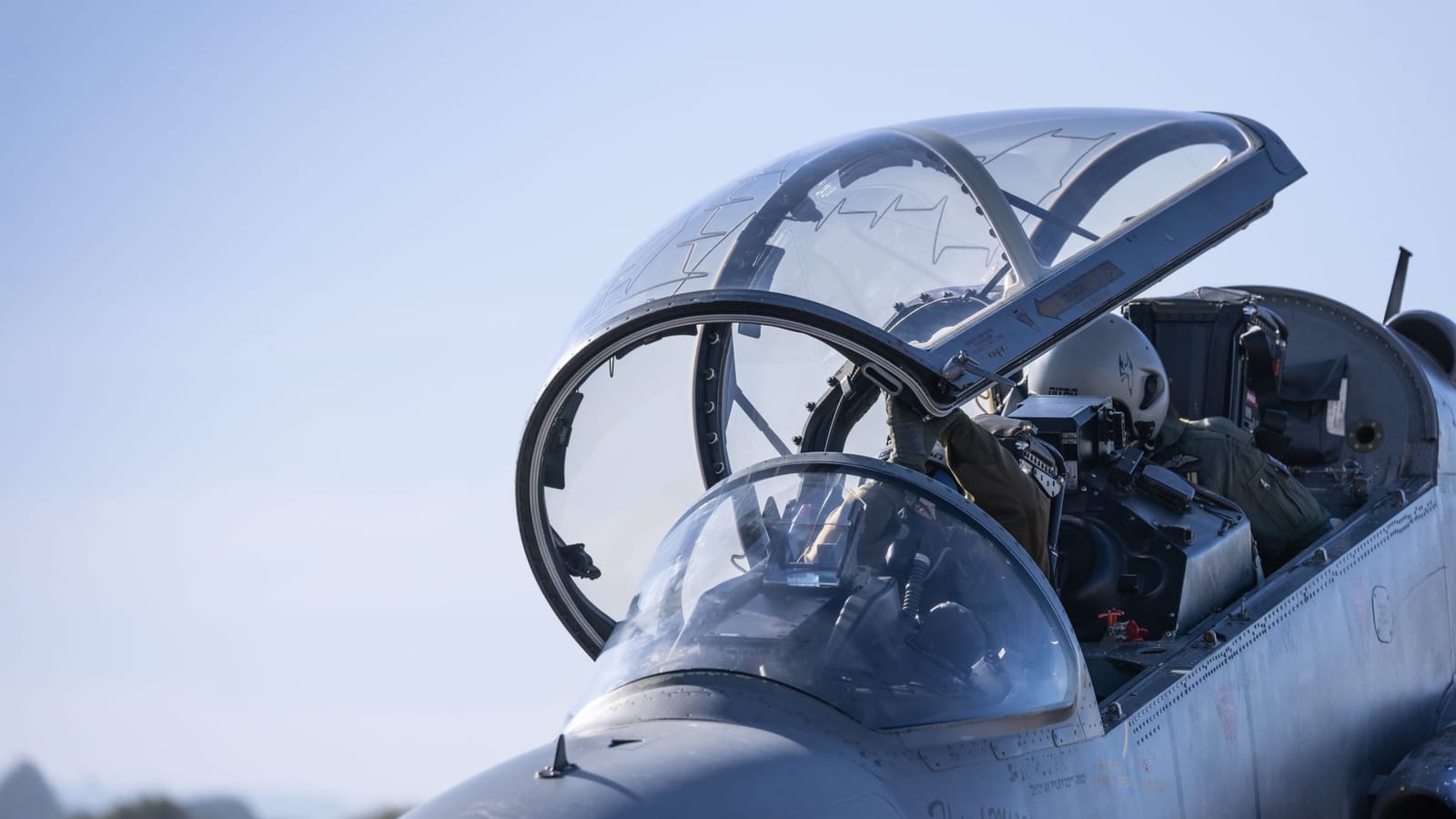 Detailed view of a military jet cockpit with pilots preparing for flight against a clear sky.