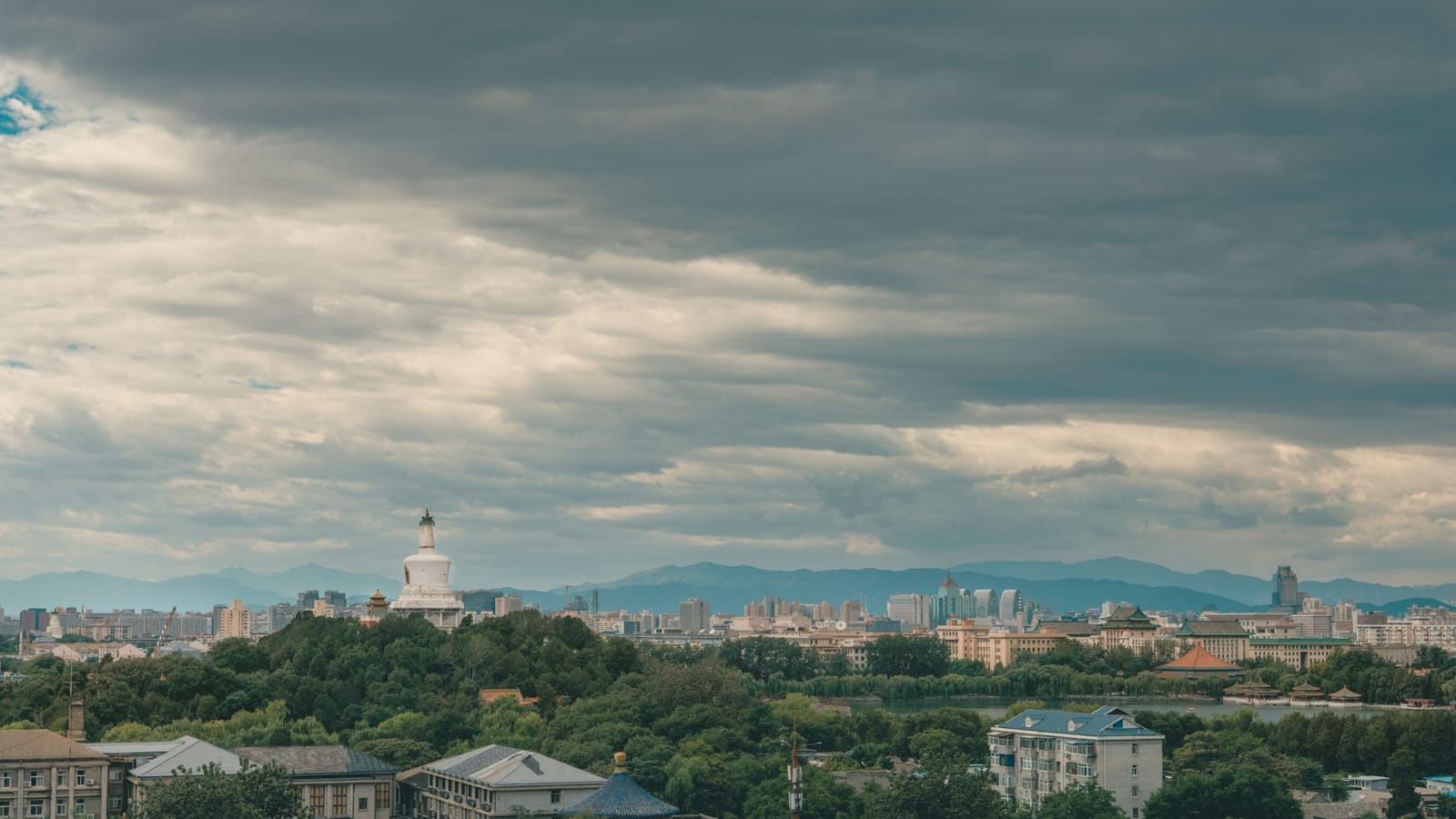 Panoramic view of Beijing with the iconic White Dagoba stupa under a cloudy sky.