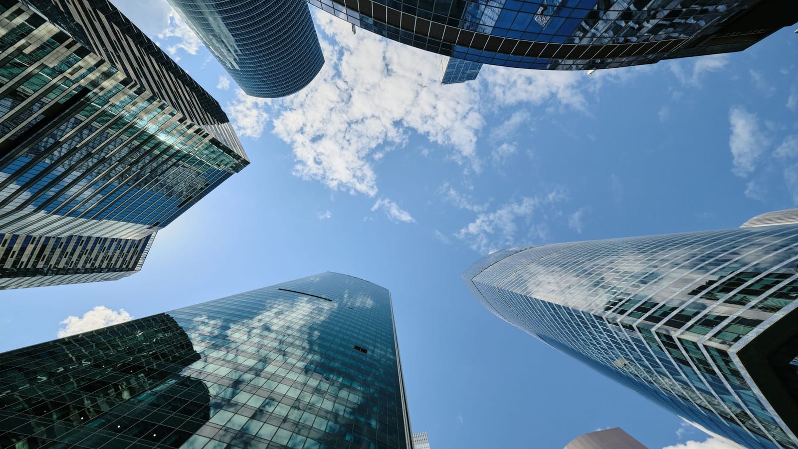A captivating upward view of modern skyscrapers against a bright blue sky with clouds.
