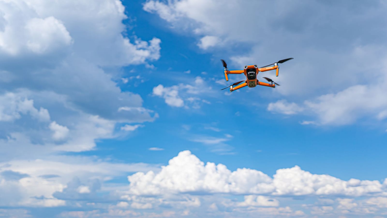 Drone flying mid-air against a vibrant blue sky with fluffy clouds, showcasing modern technology and aerial photography.