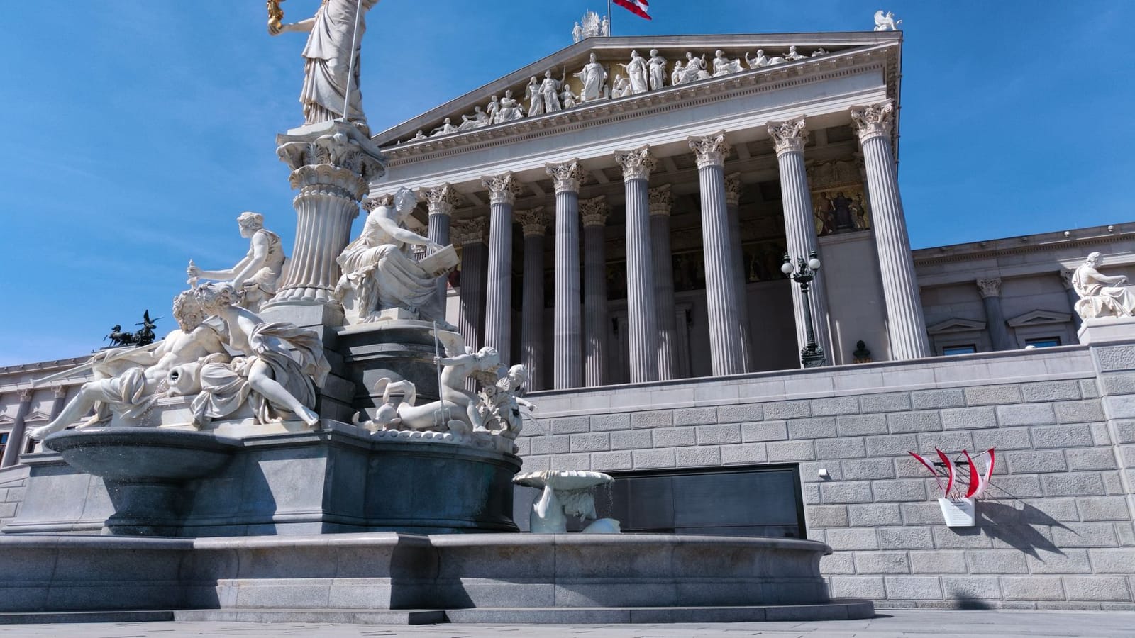 The majestic Athena Fountain outside the historic Vienna Parliament Building on a sunny day.