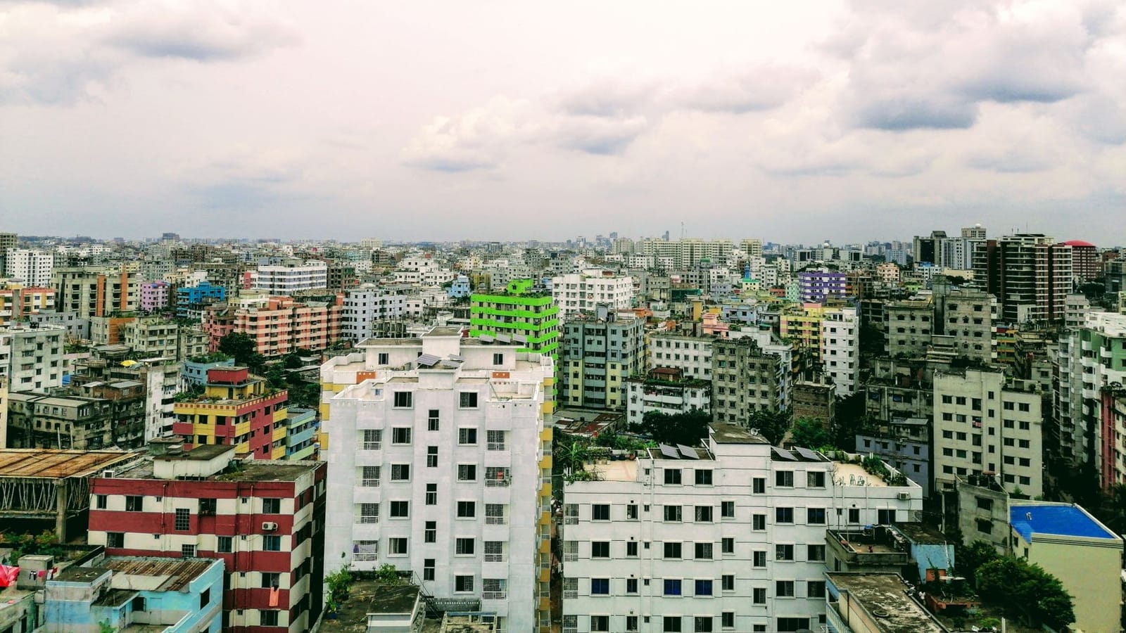 Aerial view of Dhaka's urban landscape under a cloud-filled sky, showcasing vibrant architecture.