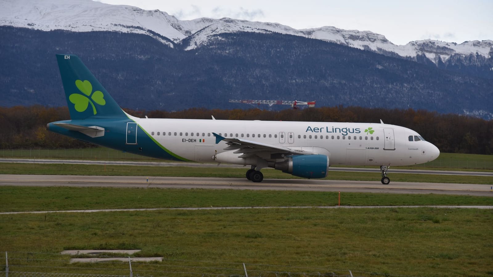 Aer Lingus aircraft taxiing at Geneva Airport with scenic mountain backdrop.