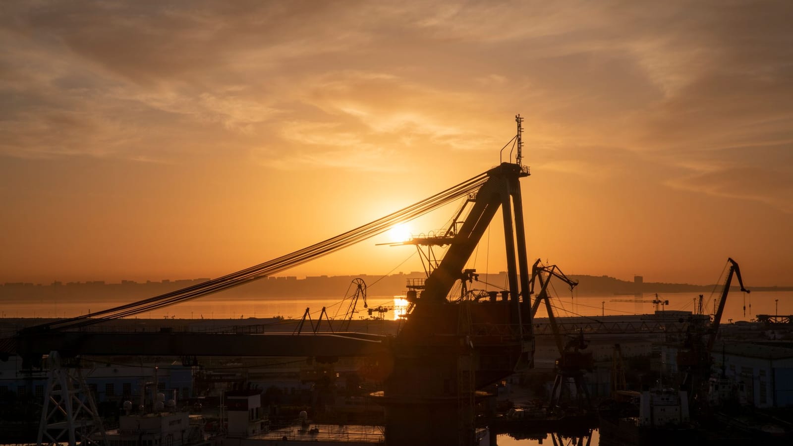 Silhouette of cranes in Baku port at sunrise, reflecting on the sea, creating a stunning industrial scene.
