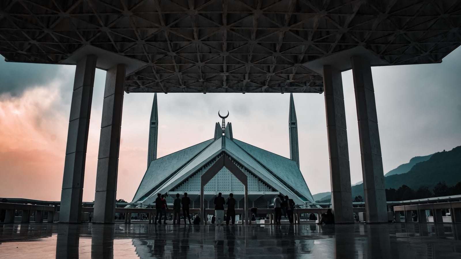A stunning view of Faisal Mosque during twilight in Islamabad, showcasing Islamic architecture with silhouetted visitors.