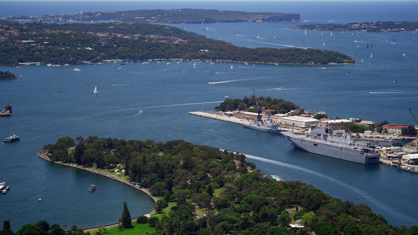 Aerial perspective of Sydney Harbour with naval ships, lush greenery, and blue waters.