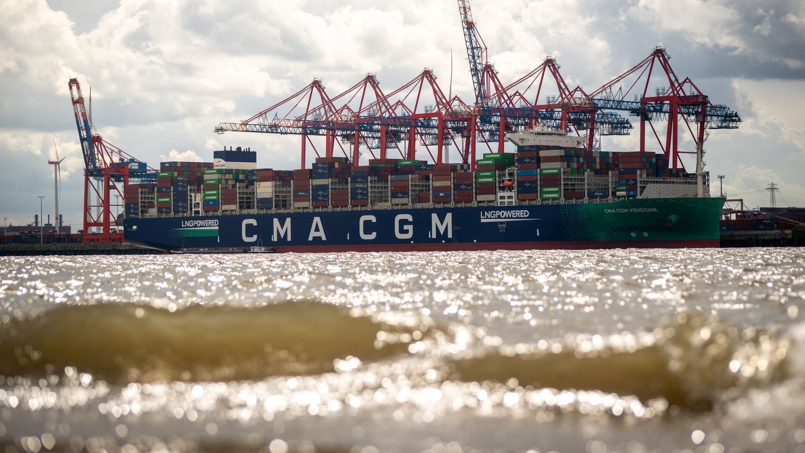Vivid view of a large CMA CGM container ship at Hamburg port, highlighting cranes and industrial activity.
