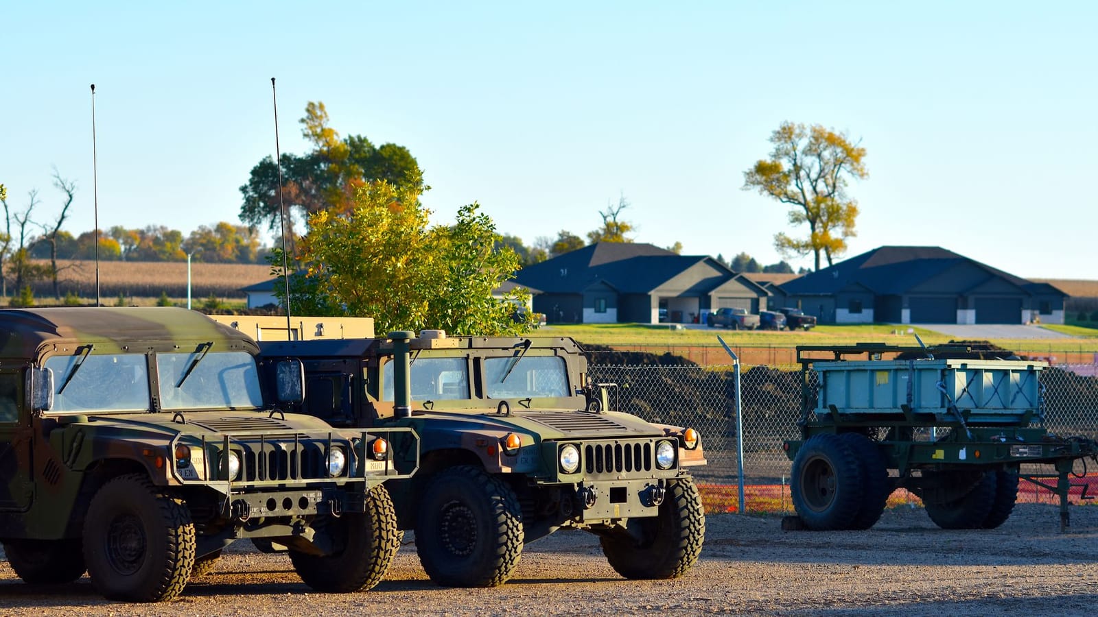 Military vehicles, including Humvees, parked outdoors near homes in autumn.