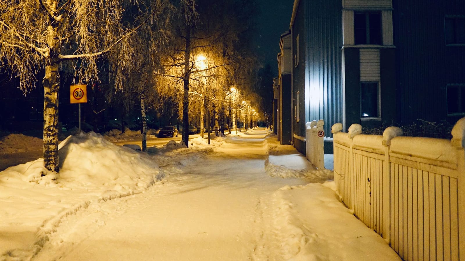 A serene snowy street in Oulu, Finland, illuminated by warm streetlights on a winter night.