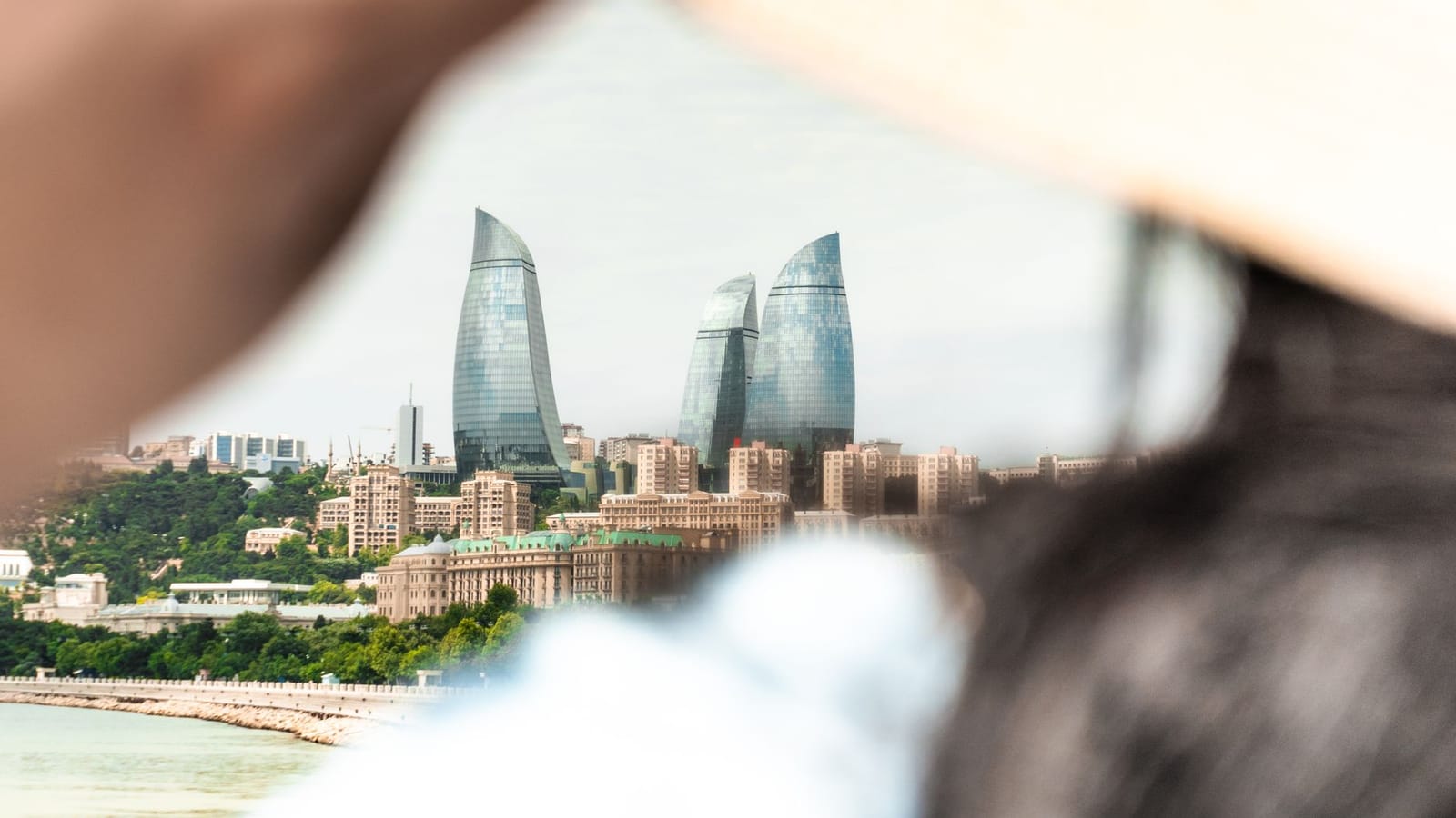 A scenic view of Baku's iconic Flame Towers seen through the perspective of a person adjusting a sunhat.