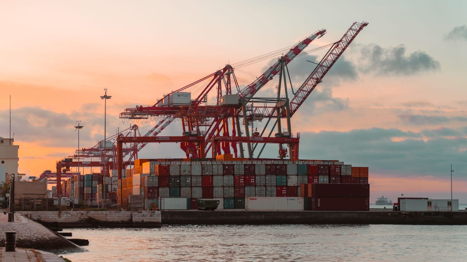 Container cranes at a bustling port during sunset, creating a vibrant industrial scene.