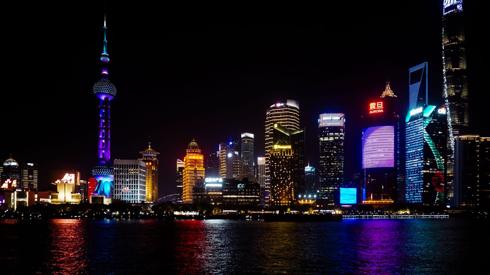 Vibrant Shanghai skyline at night featuring iconic skyscrapers and colorful lighting reflections on water.