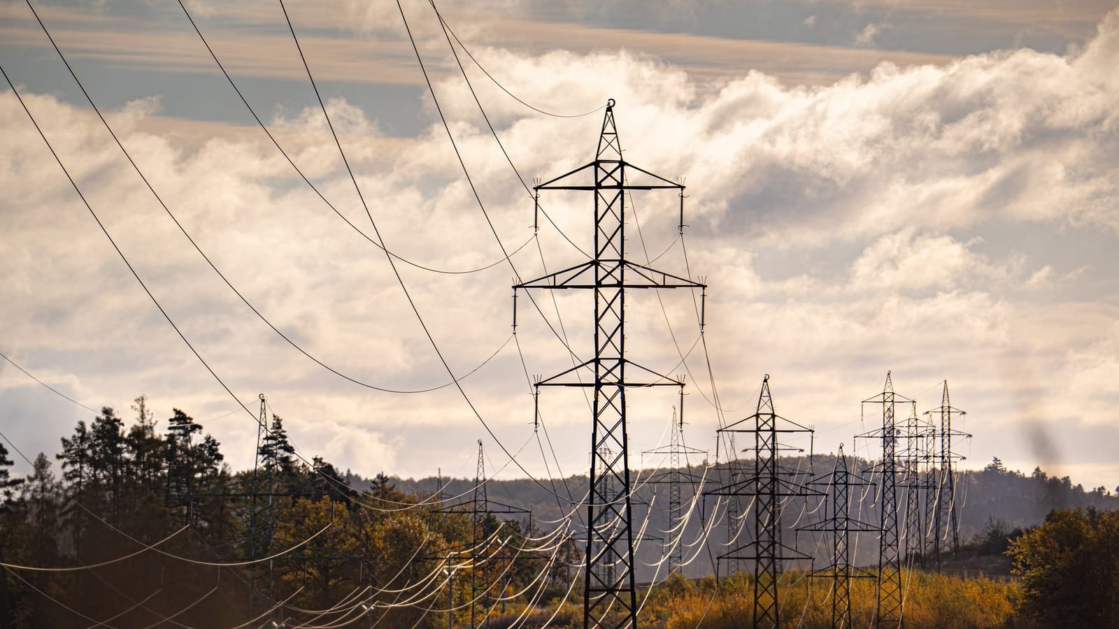 Electric pylons stretch across a picturesque autumn landscape, under a dramatic sky.