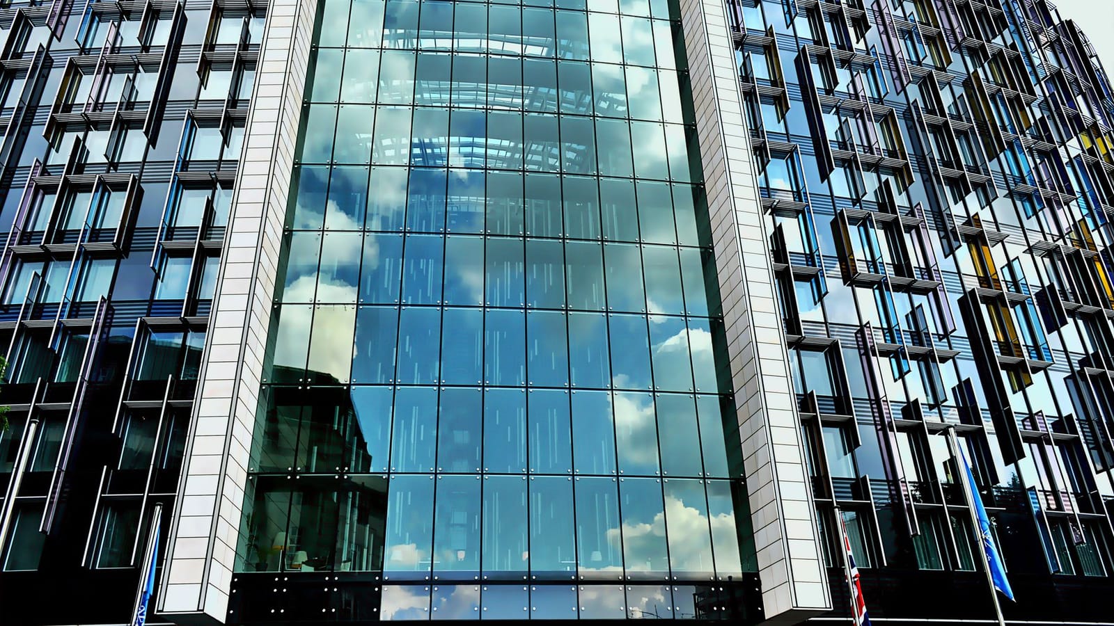 A modern skyscraper with a glass facade reflecting the blue sky and clouds.