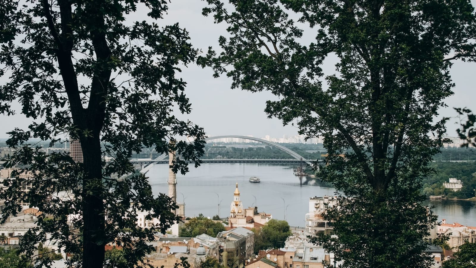A picturesque aerial shot of Kyiv with a bridge crossing the river framed by trees, capturing the city's charm.