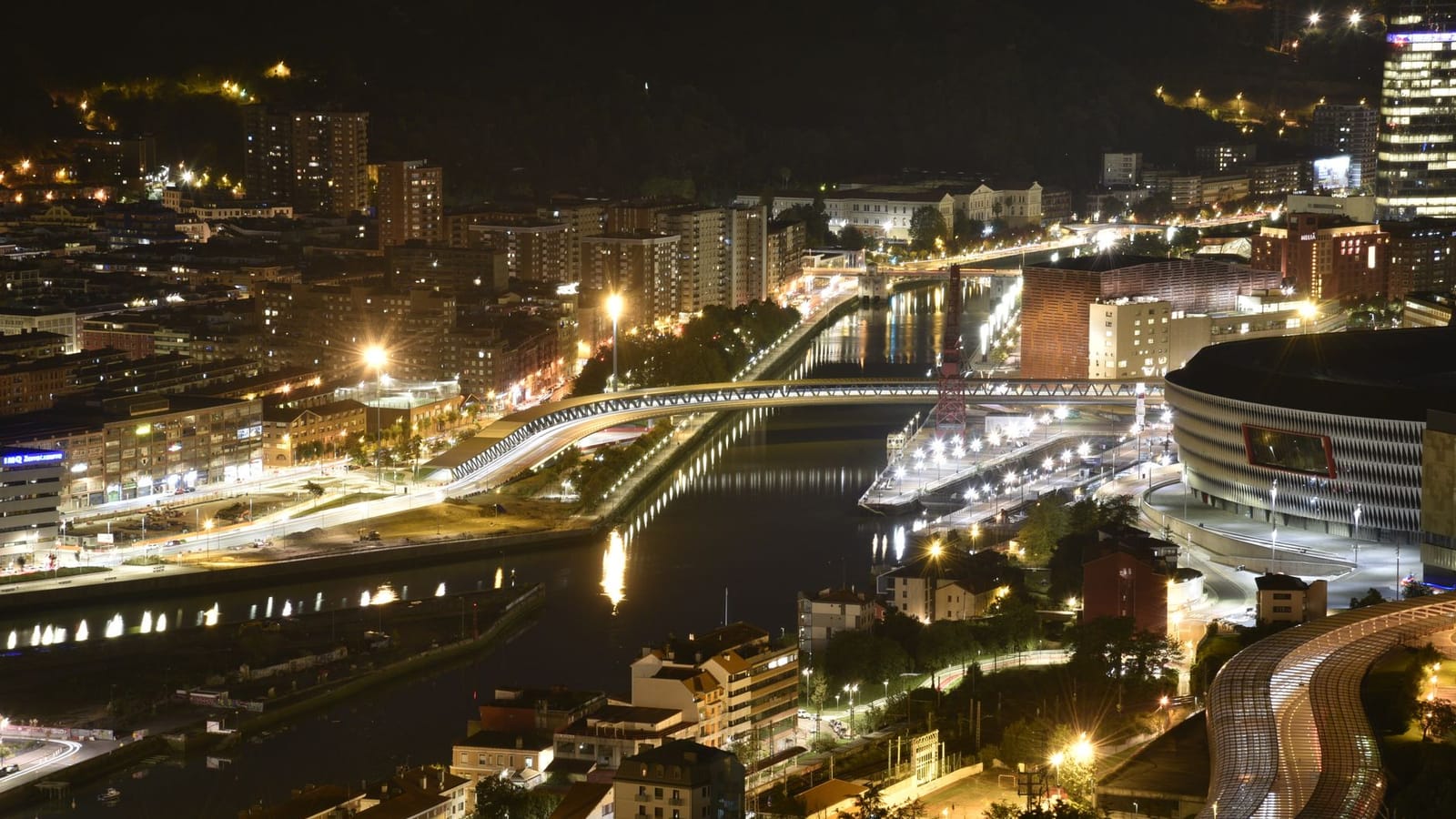 Aerial view of Bilbao cityscape illuminated at night, showcasing vibrant urban life.