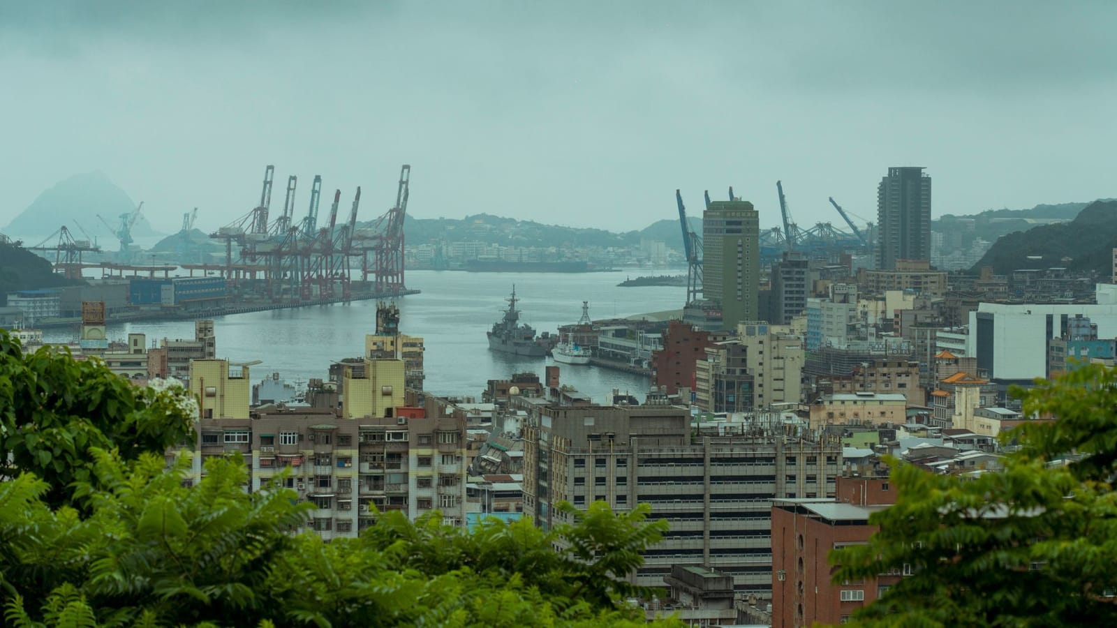 Scenic aerial view of Keelung Harbor, Taiwan with modern architecture and cranes under overcast skies.