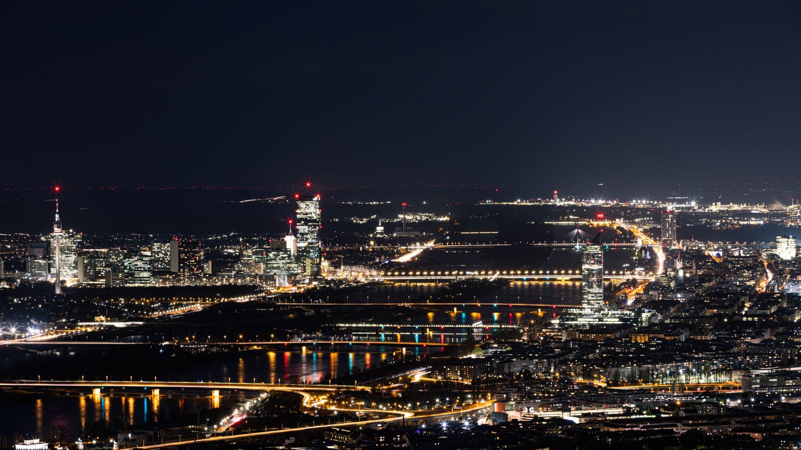 Stunning nighttime view of Vienna, Austria with illuminated cityscape and Danube River reflections.