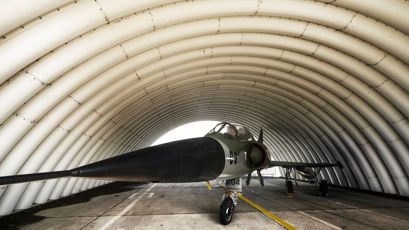 A fighter jet parked inside an arched military hangar, showcasing its sleek design.