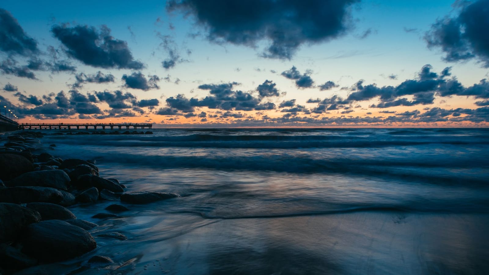 A stunning dusk view of the Baltic Sea at Palanga with clouds, waves, and a pier.