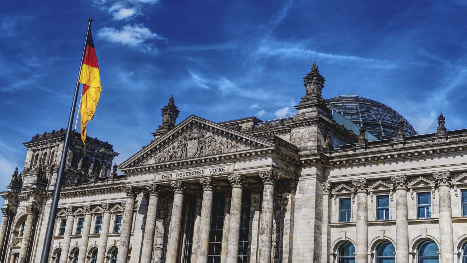 Historic Reichstag in Berlin under a vibrant blue sky, featuring the German flag.