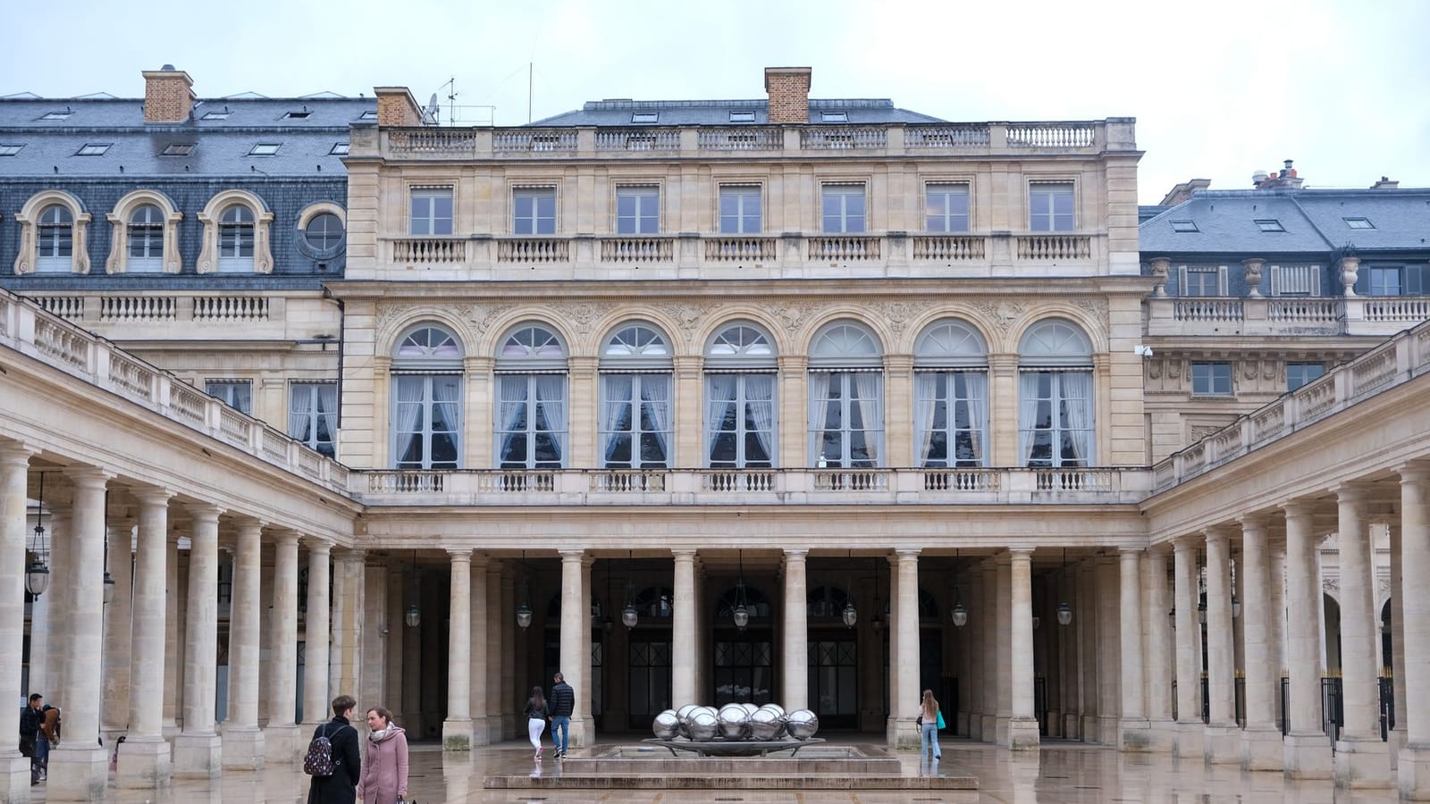 A stunning view of the historic Palais-Royal courtyard in Paris with reflective paving and classical architecture.