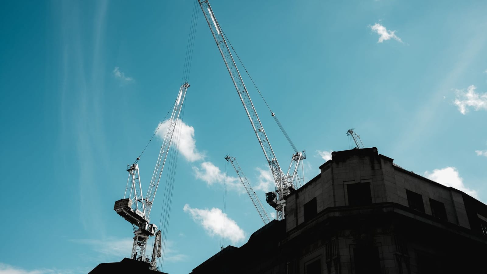 Silhouetted construction cranes extend into a clear blue sky.