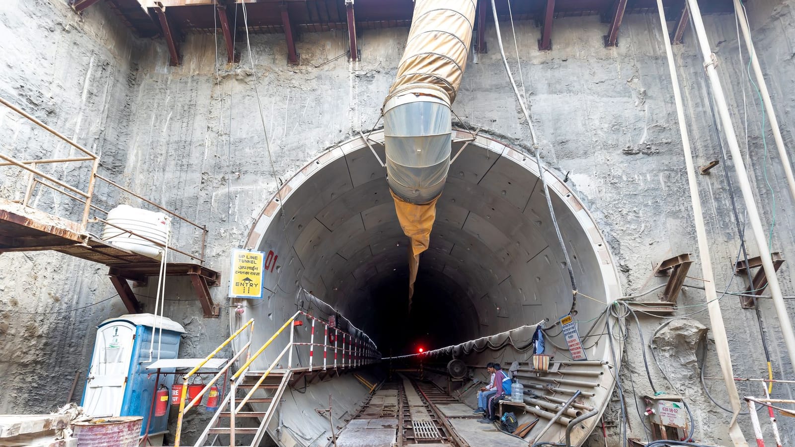 Industrial tunnel entrance under construction with heavy machinery and safety equipment.