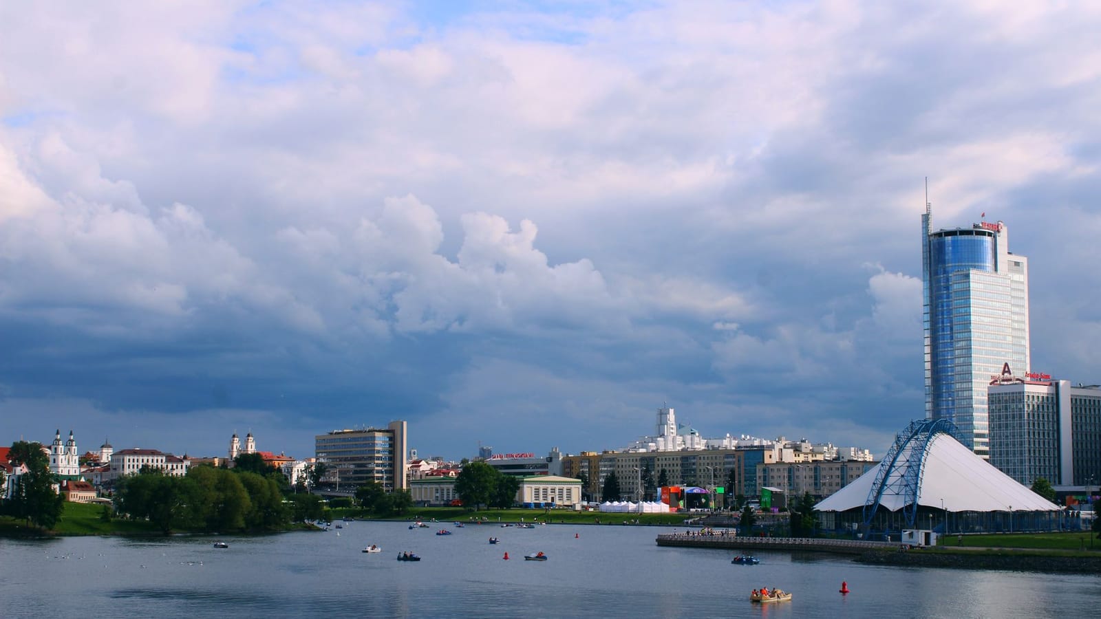 Picturesque view of Minsk cityscape along the river under a cloudy sky with modern and historic architecture.
