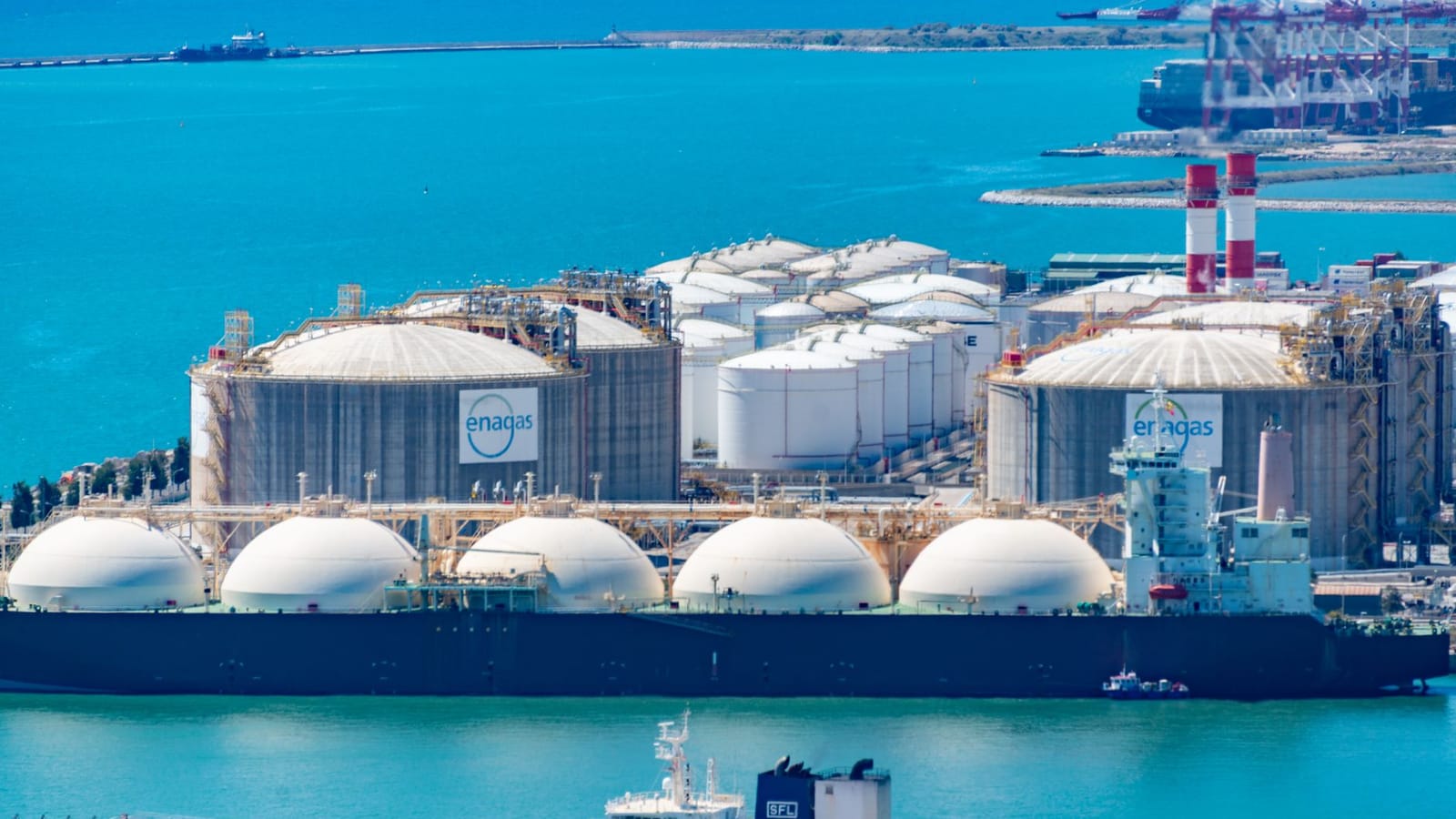 Aerial shot of a gas terminal featuring LNG storage tanks and tanker ships in turquoise waters.
